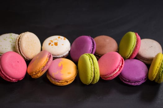 Assorted colorful french cookies macarons in a row on a dark background. Closeup. Concept of the macarons