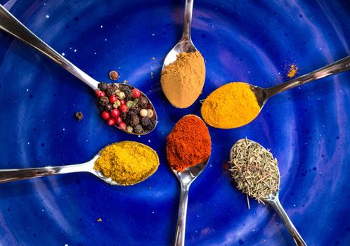 Different colorful spices in little spoons on dark blue background. Top view. Closeup