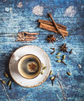 Cup of fresh hot coffee with spices on old rustic blue wooden table. Vintage background. Autumn/winter warming coffee. Black coffee, cinnamon. Espresso, white cup. Top view. Close up. From above