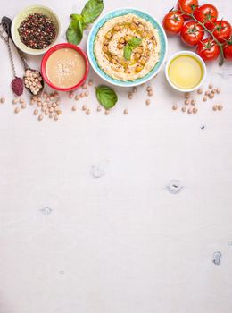 Bowl with hummus, chickpea, tahini, olive oil, sesame seeds, cherry tomatoes and herbs on white rustic wooden background. Space for text. Food frame. Middle eastern cuisine. Top view. Hummus background