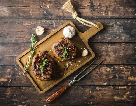 Grilled marbled meat steak Filet Mignon with seasonings, fork, wooden cutting board. Juicy meat steak. Beef steak grilled/fried. Top view. Ingredients. Prepared meat steak. Close-up. Rustic background