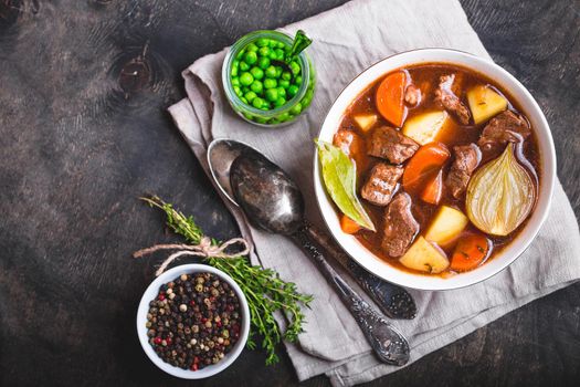 Meat stew with beef, potato, carrot, onion, spices. green peas. Slow cooked meat stew in bowl, wooden background. Hot autumn/winter dish. Closeup. Top view. Space for text. Comfort food. Homemade soup