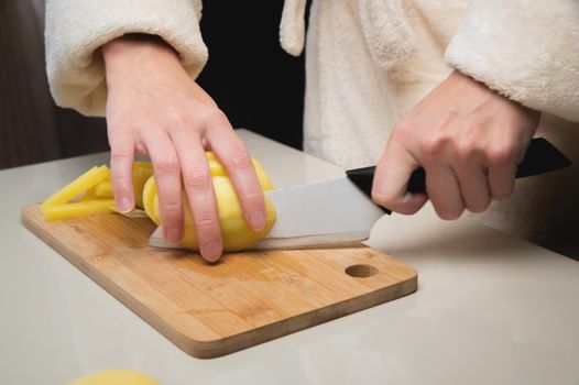 Close-up of female hands cutting peeled potatoes on a wooden cutting board. Home cooking potatoes.