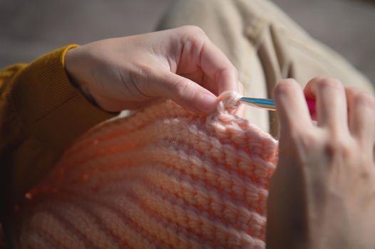 female hands close-up, crocheting clothes on the sofa at home, handmade.