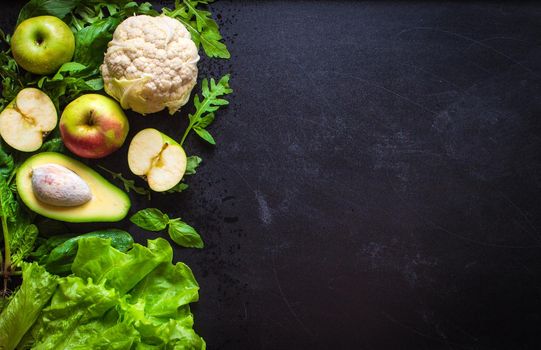 Fresh green vegetables and fruits on black chalk board background. Сauliflower, avocado, spinach, lettuce salad, green apples, herbs. Vegetarian food. Diet/healthy/detox food concept. Space for text