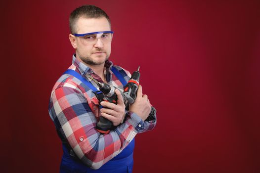 Portrait of a caucasian male repairman in a work uniform with an electric jigsaw around his neck. Studio portrait of an artisan businessman.