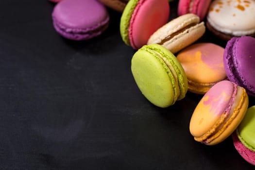 Assorted colorful french cookies macaroons on a black background. Space for text. Closeup. Top view. Concept of the baking macaroons