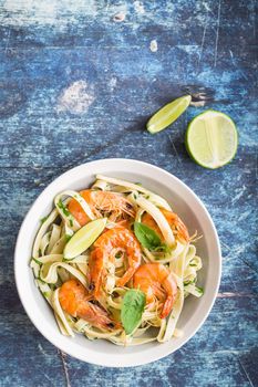 Homemade pasta with fried shrimps and basil on rustic wooden blue background. Pasta with seafood in plate. Top view. Close-up. Mediterranean cuisine. Pasta for dinner or lunch. Linguine with prawns