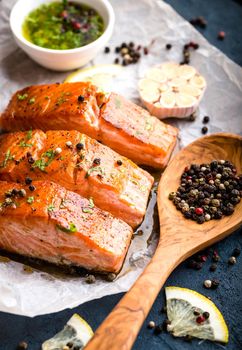 Delicious fried salmon fillet, seasonings on blue rustic concrete table. Cooked salmon steak with pepper, herbs, lemon, garlic, olive oil, spoon. Grilled fresh fish. Fish for healthy dinner. Close-up