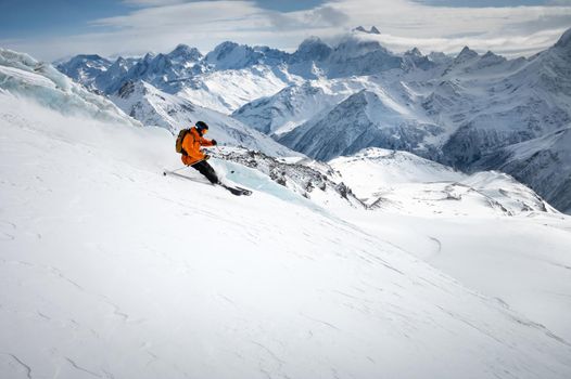 Professional skier ride at speed on a snowy slope against the backdrop of a glacier and high snow-capped mountains on a sunny day. Ski resort space copy presentation.