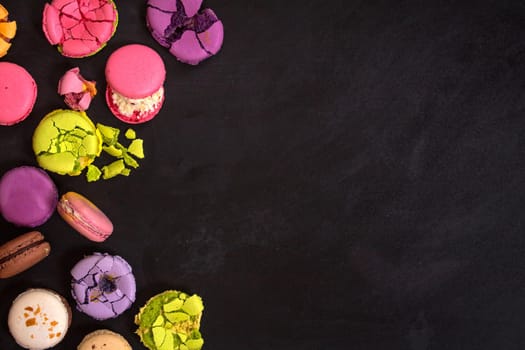 Assorted colorful french macarons on a black background. Space for text. Closeup. Top view. Concept of the baking macarons