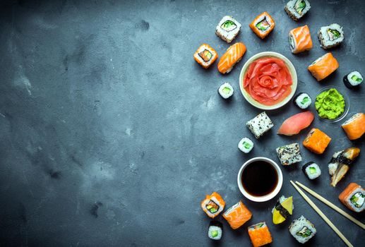 Japanese sushi on a dark background. Sushi rolls, nigiri, maki, pickled ginger, wasabi, soy sauce. Sushi set on a table. Space for text. Top view. Sushi background. Asian or Japanese food frame. Toned