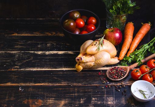 Raw whole chicken ready for cooking. Chicken, vegetables, herbs, spices on black rustic wooden background. Space for text. Food frame. Diet or healthy eating. Ingredients for cooking. Selective focus