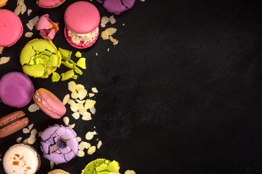 Assorted colorful french macarons and almond flakes on a black background. Space for text. Closeup. Top view. Concept of the baking macarons