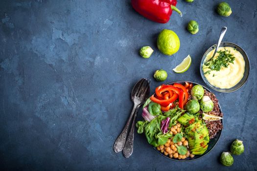 Bowl with healthy salad, dip, blue stone background. Top view. Space for text. Buddha bowl with chickpea, avocado, quinoa seeds, red bell pepper, fresh spinach, brussels sprout, lime. Vegetarian salad
