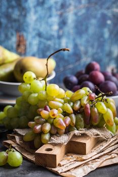 Fresh ripe grapes on wooden cutting board, pears and plums in bowls, wooden rustic background. Fresh juicy organic fruits. Close up. Organic natural fruits. Autumn/fall setting. Harvest/crop/garden