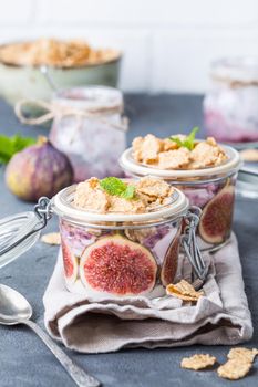 Homemade healthy yoghurt in glass pot with cereals, figs, mint on rustic concrete background. Healthy morning breakfast. Freshly made yoghurt with oat granola and fruit. Yoghurt in jar with muesli