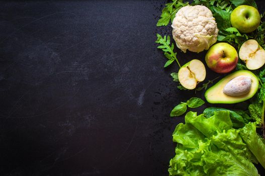 Fresh green vegetables and fruits on black chalk board background. Сauliflower, avocado, spinach, lettuce salad, green apples, herbs. Vegetarian food. Diet/healthy/detox food concept. Space for text