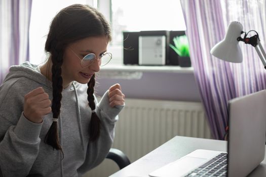 Happy girl. She checks her school test results through the internet. Young girl wearing glasses with braids.