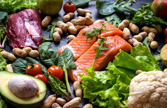 Fresh fish, meat, vegetables, fruits, nuts on black chalk board background. Сauliflower, avocado, apples, tomatoes, salmon, beef, spinach, herbs. Diet/healthy/paleo food. Ingredients for cooking