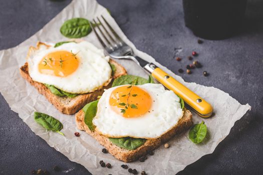 Healthy sandwich with wholegrain toast, fried egg, fresh spinach, thyme on rustic stone background. Egg sandwich for morning breakfast. Clean healthy eating concept. Vegetarian lunch/snack. Close-up