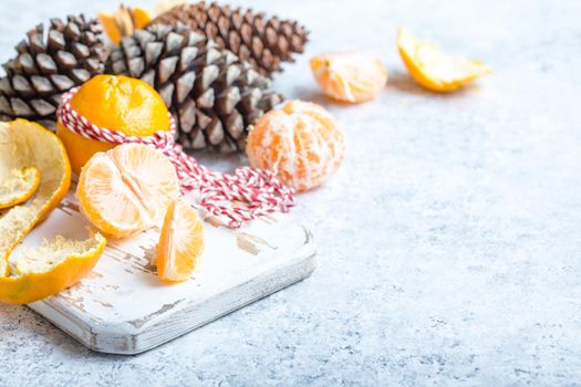 Winter white christmas background, tangerines, pine cones. Peeled tangerine, white cooking board. New Year/Xmas festive background. Winter holidays. Decoration, celebration Christmas. Space for text