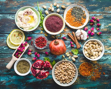 Arab ingredients for middle eastern food. Arabic cuisine ingredients on blue wooden background. Hummus, chickpea, lentils, rose buds, spices, pomegranate, pistachios. Halal food making. Top view