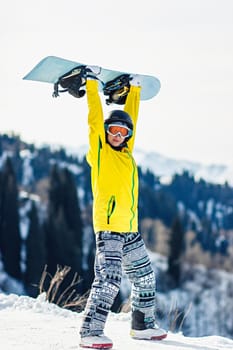 Young woman holds a snowboard over her head on a background of mountains