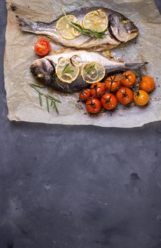 Tasty baked fish on dark rustic background. Baked sea bream with lemon, onion, herbs, tomatoes, spices. Space for text. Grilled delicious fish background. Diet and healthy food concept. Top view