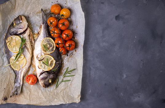 Tasty baked fish on dark rustic background. Baked sea bream with lemon, onion, herbs, tomatoes, spices. Space for text. Grilled delicious fish background. Diet and healthy food concept. Top view