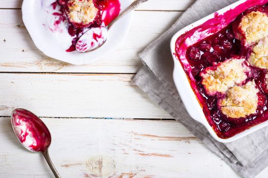 Homemade cherry cobbler pie with flaky crust, ice cream, vintage spoon, sieve for flour. Top view on the white wooden table background. Space for text