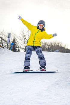 Beautiful young woman in black helmet and yellow jacket learns to snowboard ride
