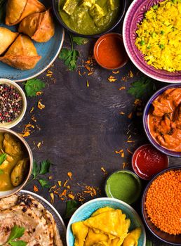 Assorted indian food on dark wooden background. Dishes of indian cuisine. Curry, butter chicken, rice, lentils, paneer, samosa, naan, chutney, spices. Space for text. Bowls and plates with indian food