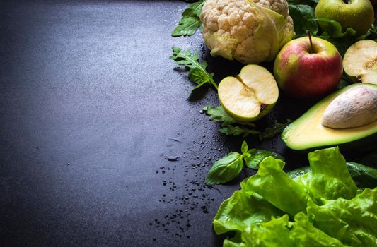 Fresh green vegetables and fruits on black chalk board background. Сauliflower, avocado, spinach, lettuce salad, green apples, herbs. Vegetarian food. Diet/healthy/detox food concept. Space for text