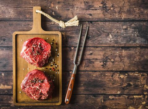 Raw marbled meat steak Filet Mignon with seasonings, fork, wooden cutting board. Space for text. Beef steak ready for cooking. Top view. Ingredients. Uncooked meat steak. Close-up. Rustic background