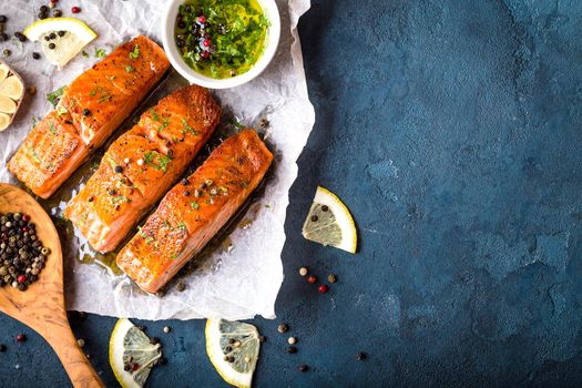 Delicious fried salmon fillet, seasonings on blue rustic concrete background. Cooked salmon steak with pepper, herbs, lemon, garlic, olive oil, spoon. Space for text. Fish for dinner. Healthy eating