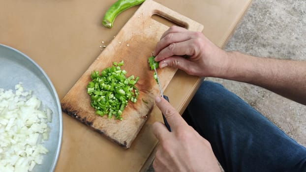 Man cuts vegetables on cutting board for picnic. Process of making salad outdoors, hands close-up.