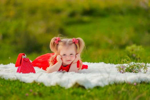 a girl in a red dress lies on a white blanket that is laid on the lawn