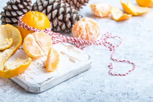 Winter white christmas background, tangerines, pine cones. Peeled tangerine, white cooking board. New Year/Xmas festive background. Winter holidays. Decoration, celebration Christmas. Space for text