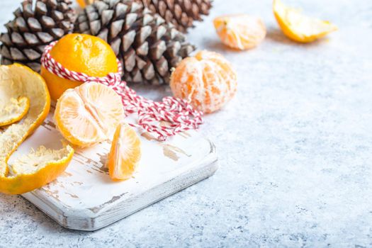 Winter white christmas background, tangerines, pine cones. Peeled tangerine, white cooking board. New Year/Xmas festive background. Winter holidays. Decoration, celebration Christmas. Space for text