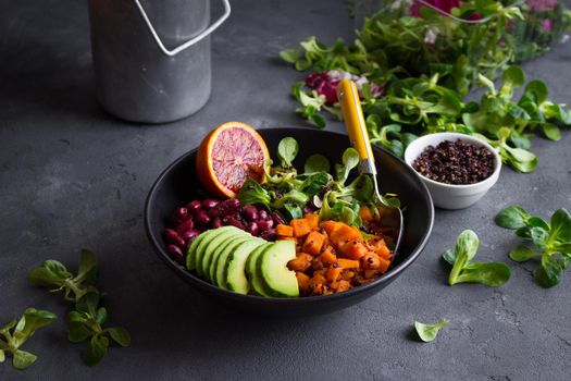 Quinoa salad in bowl with avocado, sweet potato, beans, herbs, orange on concrete rustic background. Quinoa superfood concept. Clean healthy detox eating. Vegan/vegetarian food. Making healthy salad