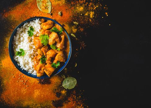 Indian Butter chicken with basmati rice in bowl, spices, black background. Space for text. Butter chicken, traditional Indian dish. Top view. Chicken tikka masala. Indian cuisine concept. Overhead