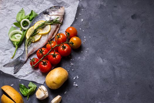 Raw fish with fresh ingredients ready to cook. Fish, lemon, herbs, potato, tomatoes. Ingredients for cooking on dark rustic background. Space for text. Diet and healthy food. Fish background. Top view