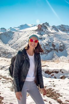 A happy girl in glasses smiles against the background of snow mountain peaks.