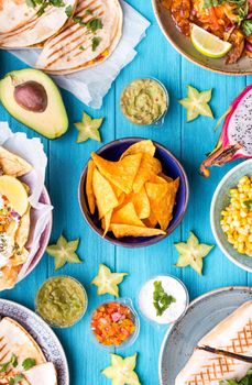 Assorted mix of traditional Mexican food. Different Mexican dishes table. Cheese nachos, tacos, guacamole, quesadilla, burrito, fajitas, tortilla chips, Mexican fruits. Tex-Mex cuisine. Mexico style