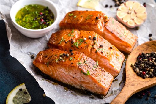 Delicious fried salmon fillet, seasonings on blue rustic concrete table. Cooked salmon steak with pepper, herbs, lemon, garlic, olive oil, spoon. Grilled fresh fish. Fish for healthy dinner. Close-up