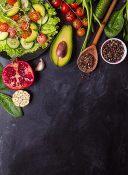 Ingredients for making salad on rustic black chalk board background. Vegetable salad in bowl, avocado, tomato, cucumber, spinach. Healthy, clean eating concept. Vegan or gluten free diet. Copy space