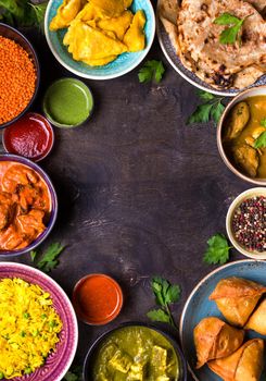 Assorted indian food on dark wooden background. Dishes of indian cuisine. Curry, butter chicken, rice, lentils, paneer, samosa, naan, chutney, spices. Space for text. Bowls and plates with indian food