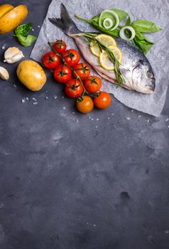 Raw fish with fresh ingredients ready to cook. Fish, lemon, herbs, potato, tomatoes. Ingredients for cooking on dark rustic background. Space for text. Diet and healthy food. Fish background. Top view