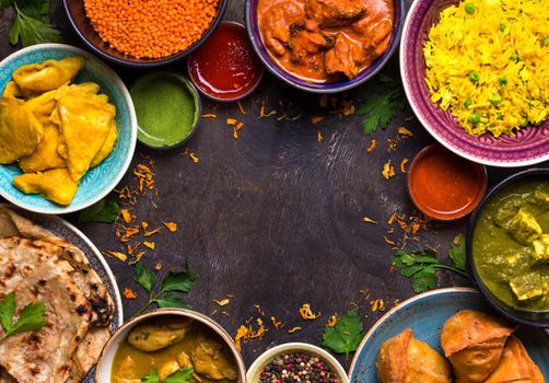 Assorted indian food on dark wooden background. Dishes of indian cuisine. Curry, butter chicken, rice, lentils, paneer, samosa, naan, chutney, spices. Space for text. Bowls and plates with indian food